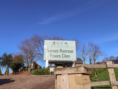 A sign reading Sunset Retreat Foxes Den at Riggs Head Farm with trees and buildings in the background at Foxes Den in Seamer North Yorkshire