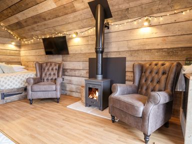 A room with two armchairs a wood stove a wall mounted tv and a bed at Sunset Retreat in Seamer North Yorkshire