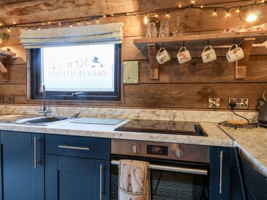 A kitchen with blue cabinets a marble countertop a sink an oven and hanging mugs at Sunset Retreat in Seamer North Yorkshire