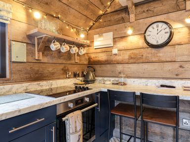 A kitchen corner with wooden walls a stove oven kettle hanging mugs glass jars and two chairs at Sunset Retreat in Seamer North Yorkshire