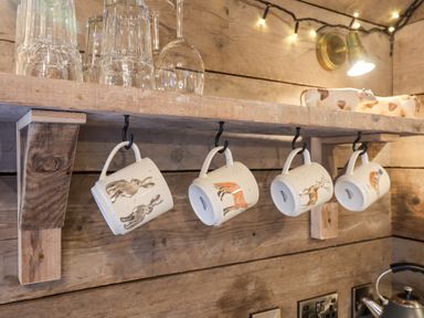 A wooden shelf with hanging animal-themed mugs glassware on top and a kettle below at Sunset Retreat in Seamer North Yorkshire