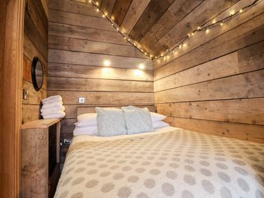 A bedroom with wooden walls a bed with pillows and a blanket and string lights at Sunset Retreat in Seamer North Yorkshire