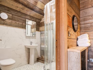 A bathroom with a toilet sink shower wooden walls and folded towels on a wooden shelf at Sunset Retreat in Seamer North Yorkshire