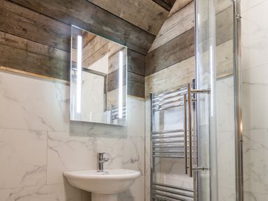 A bathroom with a sink a mirror with lights wooden walls and a glass shower enclosure at Sunset Retreat in Seamer North Yorkshire