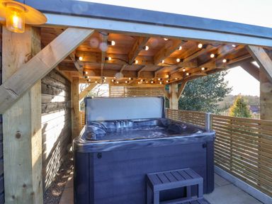 An outdoor hot tub under a wooden pergola with string lights on the ceiling at Sunset Retreat in Seamer North Yorkshire