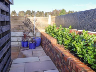 An outdoor patio area with potted plants and a raised brick planter with green shrubs at Sunset Retreat in Seamer North Yorkshire