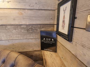 A wooden corner with a framed picture of a hare a black information folder and a leather corner of a sofa at Sunset Retreat in Seamer North Yorkshire