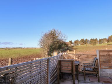 A fenced patio with wooden chairs and a table overlooking open fields and trees at Sunset Retreat in Seamer North Yorkshire