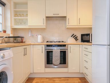 A kitchen with white cabinets a washing machine a stove oven a refrigerator microwave and knives at 1 Bethany Court in Bodmin