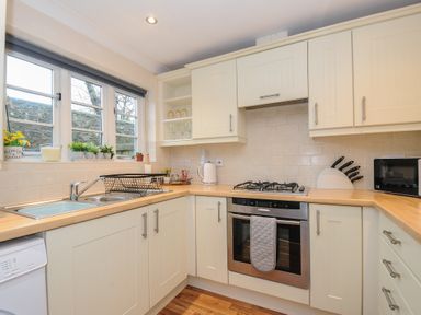 A kitchen with cream cabinets a sink oven gas stove knives and microwave at 1 Bethany Court in Bodmin