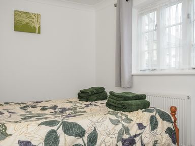 A bedroom with a bed covered in leaf-patterned bedding and green towels on top at 1 Bethany Court in Bodmin