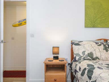 A bedroom with a wooden bedside table and lamp next to a bed with leaf-patterned bedding at 1 Bethany Court in Bodmin