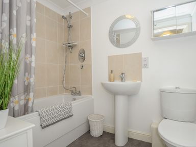 A bathroom with a bathtub shower combination a sink with a mirror and a toilet at 1 Bethany Court in Bodmin