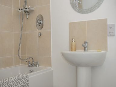 A bathroom with a bathtub and shower next to a pedestal sink with a soap dispenser and bar of soap at 1 Bethany Court in Bodmin
