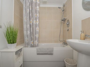 A bathroom with a bathtub shower combination and a floral shower curtain at 1 Bethany Court in Bodmin