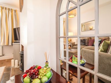 A living room with a sofa and pillows reflected in a mirror and a bowl of fruit on a table at Quarrier's Rest in Swanage