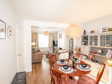 A dining area with a wooden table set for four and a living room with sofas and a television at Quarrier's Rest in Swanage