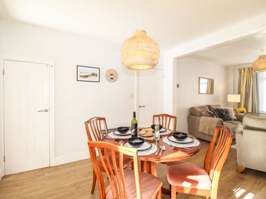 A dining area with a wooden table set for four and a living room with sofas and a lamp at Quarrier's Rest in Swanage