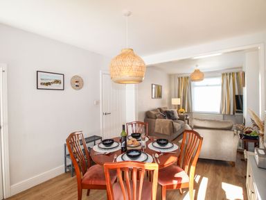 A dining area with a round table set for four and a living room with sofas and a window at Quarrier's Rest in Swanage