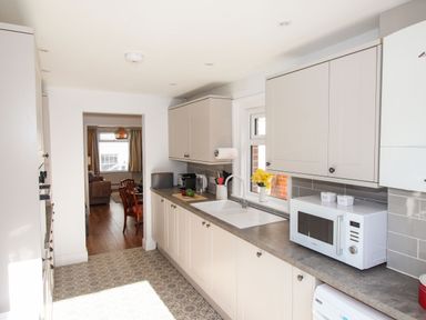 A kitchen with white cabinets a microwave a sink and a view into a dining area at Quarrier's Rest in Swanage