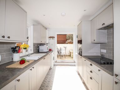 A kitchen with white cabinets, gray countertops, a sink, microwave, stove, and a door leading to an outdoor patio at Quarrier's Rest in Swanage