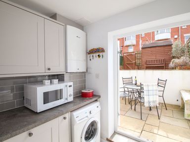 A kitchen with cabinets microwave washing machine and a door leading to a patio with a table and chairs at Quarrier's Rest in Swanage