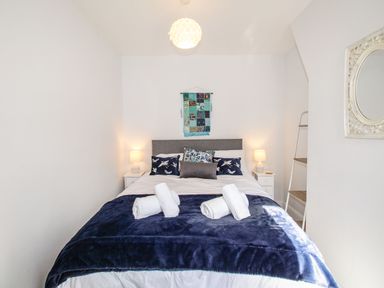 A bedroom with a bed with pillows and rolled towels on a blanket two bedside tables with lamps and a wall hanging above the bed at Quarrier's Rest in Swanage