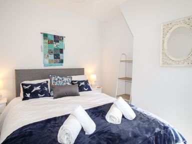A bedroom with a bed with pillows and rolled towels a wall hanging and a mirror at Quarrier's Rest in Swanage