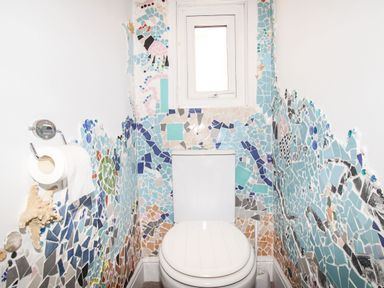 A small bathroom with a white toilet and mosaic tiled walls with sea-themed designs at Quarrier's Rest in Swanage