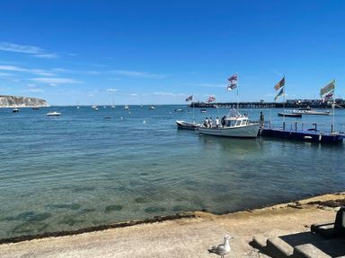 A harbor with boats anchored and a pier with flags and people by the water at Quarrier's Rest in Swanage
