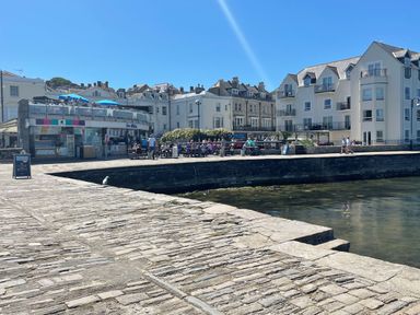 A stone paved waterfront area with people sitting at outdoor tables near white buildings at Quarrier's Rest in Swanage