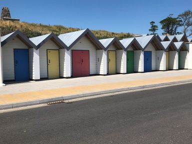 A row of small beach huts with colorful doors along a paved walkway at Quarrier's Rest in Swanage