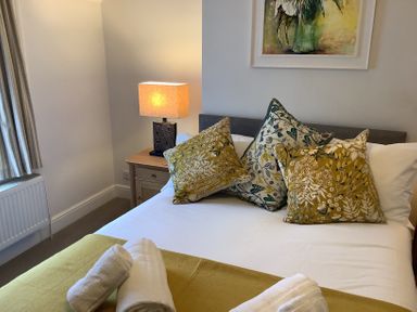A bedroom with a bed made with white sheets pillows and towels on a blanket a bedside table with a lamp and a painting above the bed at Quarrier's Rest in Swanage