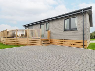 An exterior view of a single story building with a wooden deck and paved driveway at Mordros Lodge in St Day