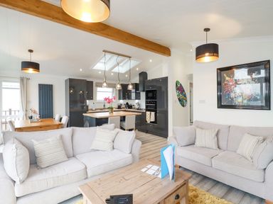 An open living room and kitchen with sofas coffee table dining table and modern cabinets at Mordros Lodge in St Day