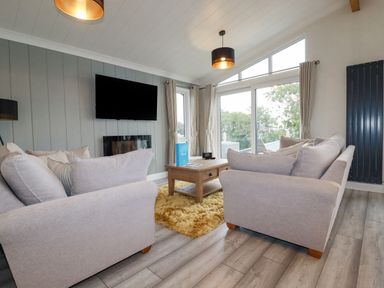 A living room with two sofas a wooden coffee table a wall-mounted television and large windows at Mordros Lodge in St Day