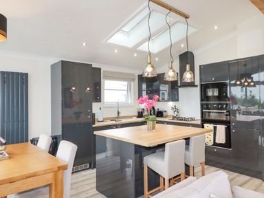 A kitchen with a wooden island, gray cabinets, hanging lights, and a dining table at Mordros Lodge in St Day