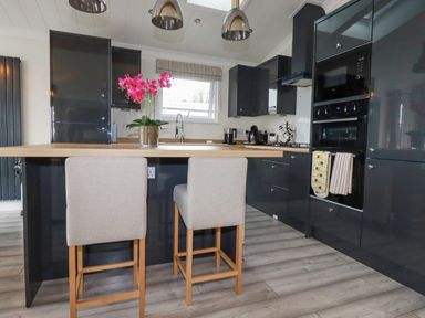 A kitchen with bar stools and a flower vase on the island at Mordros Lodge in St Day