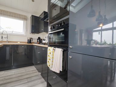 A kitchen with black cabinets a built in oven kettle coffee machine and a window at Mordros Lodge in St Day