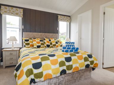 A bedroom with a patterned bedspread and pillows a bedside table with a lamp and stacked blue towels on the bed at Mordros Lodge in St Day