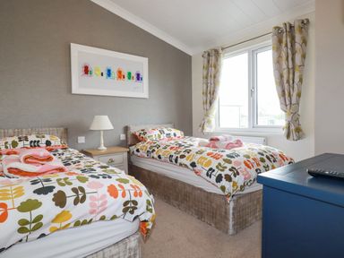 A bedroom with two single beds floral bedding a bedside table lamp a window with curtains and a blue dresser at Mordros Lodge in St Day