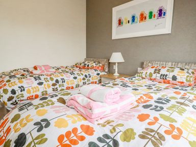 A bedroom with two single beds with floral bedding a bedside table with a lamp and towels on the beds at Mordros Lodge in St Day