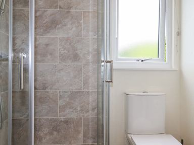 A bathroom with a shower with tiled walls and a toilet next to a frosted window at Mordros Lodge in St Day