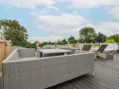 An outdoor deck with wicker seating including a sofa, chairs, a table, and two lounge chairs at Mordros Lodge in St Day