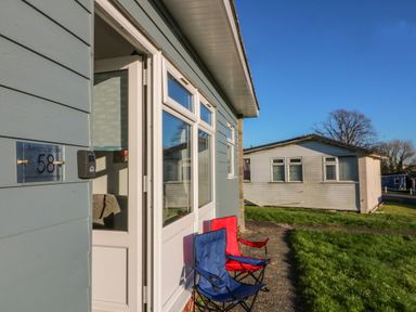 Front exterior of a holiday chalet with two folding chairs on a path by the door at Beachcomber Norton Park near Dartmouth