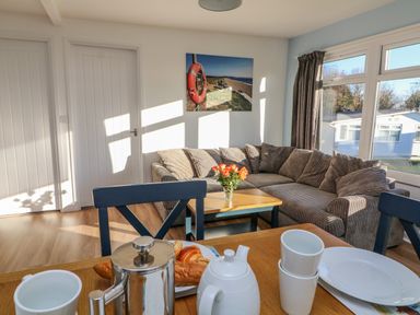 A living room with a grey striped corner sofa a wooden coffee table with flowers and a dining table set with white cups plates and a stainless steel coffee pot at Beachcomber Norton Park near Dartmouth