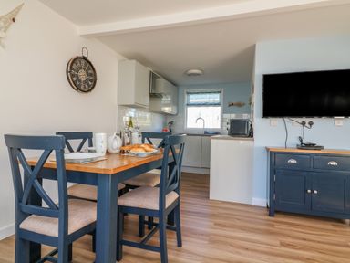 A dining area with a wooden table and four chairs next to a kitchen and a wall-mounted TV at Beachcomber Norton Park near Dartmouth