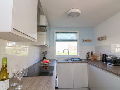 A kitchen with a sink under a window a stove a bottle of wine and two glasses on the counter at Beachcomber Norton Park near Dartmouth