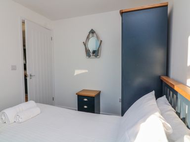 A bedroom with a bed with white sheets and pillows two rolled towels a nightstand a door and a wardrobe with a mirror on the wall at Beachcomber Norton Park near Dartmouth