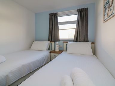 A bedroom with two single beds a window with curtains and a nightstand between the beds at Beachcomber in Norton Park near Dartmouth